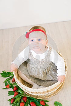 Little cute girl 1 year old in a wicker basket decorated with red juicy strawberries. Healthy eating