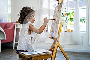 Little cute girl artist painting picture on canvas with watercolor paints at home