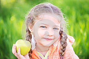 Little cute girl on a background of green grass with an apple