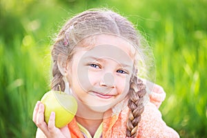 Little cute girl on a background of green grass with an apple