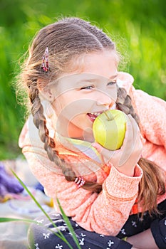 Little cute girl on a background of green grass with an apple