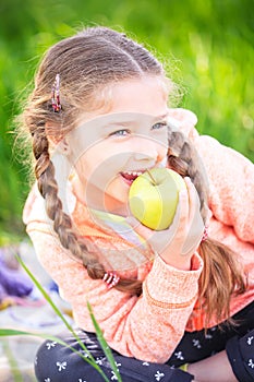 Little cute girl on a background of green grass with an apple