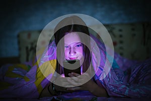 Little cute girl in bed at night under a blanket looking at the smartphone.