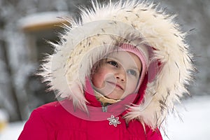 Little cute girl in a big fur hood thinks about something good