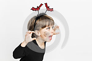 Little cute girl in black clothes and bat hoop. Scary face. Between pumpkins. Halloween celebration. White background. Minimalist
