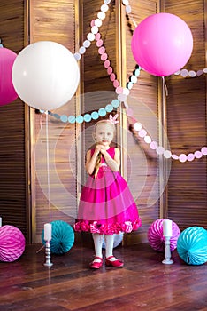 Little cute girl with blond hair in a pink dress and a princess crown with large bright balloons and garlands. Children`s holiday.