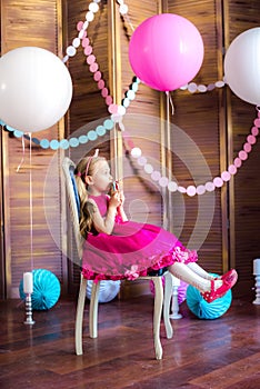 Little cute girl with blond hair in a pink dress and a princess crown with large bright balloons and garlands. Children`s holiday.