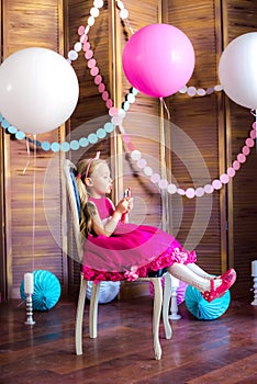 Little cute girl with blond hair in a pink dress and a princess crown with large bright balloons and garlands. Children`s holiday.