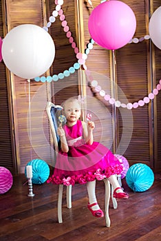 Little cute girl with blond hair in a pink dress and a princess crown with large bright balloons and garlands. Children`s holiday.