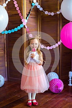 Little cute girl with blond hair in a pink dress and a princess crown with large bright balloons and garlands. Children`s holiday.