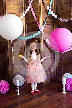 Little cute girl with blond hair in a pink dress and a princess crown with large bright balloons and garlands. Children`s holiday.