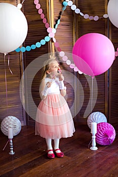 Little cute girl with blond hair in a pink dress and a princess crown with large bright balloons and garlands. Children`s holiday.