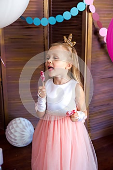 Little cute girl with blond hair in a pink dress and a princess crown with large bright balloons and garlands. Children`s holiday.