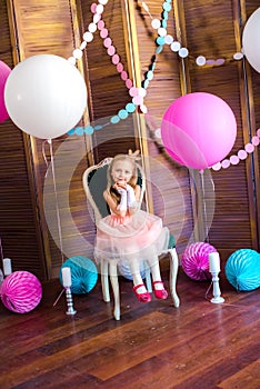 Little cute girl with blond hair in a pink dress and a princess crown with large bright balloons and garlands. Children`s holiday.