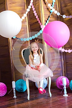 Little cute girl with blond hair in a pink dress and a princess crown with large bright balloons and garlands. Children`s holiday.