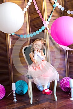 Little cute girl with blond hair in a pink dress and a princess crown with large bright balloons and garlands. Children`s holiday.