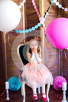 Little cute girl with blond hair in a pink dress and a princess crown with large bright balloons and garlands. Children`s holiday.