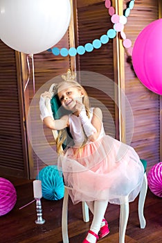 Little cute girl with blond hair in a pink dress and a princess crown with large bright balloons and garlands. Children`s holiday.