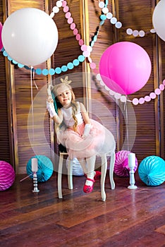 Little cute girl with blond hair in a pink dress and a princess crown with large bright balloons and garlands. Children`s holiday.