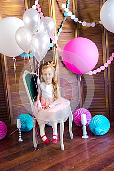 Little cute girl with blond hair in a pink dress and a princess crown with large bright balloons and garlands. Children`s holiday.