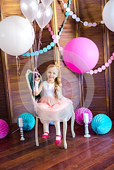 Little cute girl with blond hair in a pink dress and a princess crown with large bright balloons and garlands. Children`s holiday.