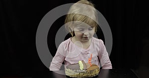 Little cute girl blows out festive candle on birthday cake on black background
