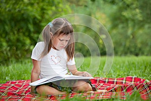 Little cute girl with book on plaid in park