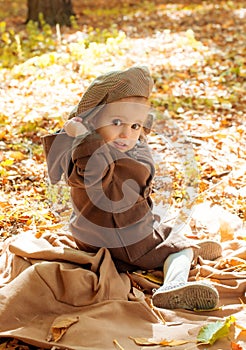 Little cute girl in a brown autumn coat in a sunny autumn park among yellow leaves. Autumn walk in the park