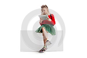 Little cute girl in casual clothes sitting on big box isolated on white studio background. Happy childhood concept.