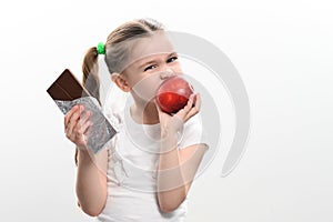 Little cute girl chooses apple over chocolate, preference of healthy food over unhealthy and unhealthy.