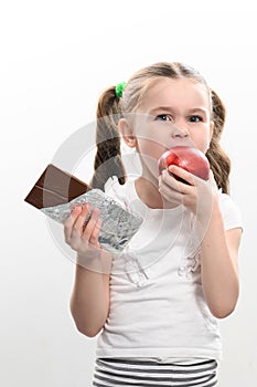 Little cute girl chooses apple over chocolate, preference of healthy food over unhealthy and unhealthy.
