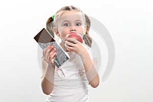 Little cute girl chooses apple over chocolate, preference of healthy food over unhealthy and unhealthy.