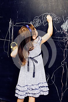 Little cute girl in classroom at blackboard writing smiling, preschooler from back alone, lifestyle people concept