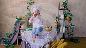 Little cute girl cook sitting in the kitchen smiling, playing with food.