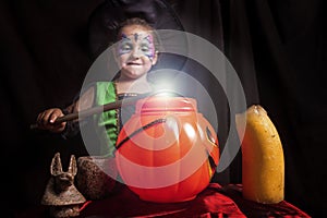 Little cute girl costumed as a witch spells a sweet pumpkin