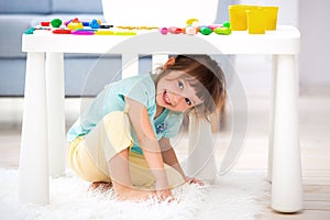 Little cute girl crawled under the table. The kid smiles, plays hide and seek