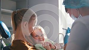 Little cute girl in the dentist`s office does not want to be treated, resisting and closing her mouth with her hands