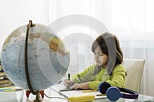 Little cute girl doing homework at home - Pre or elementary schooler girl drawing and painting the world on the school notebook