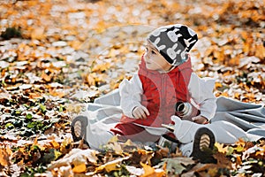 Little cute girl drinks tea from a thermos in the autumn park. Cute little toddler baby with thermos and cup