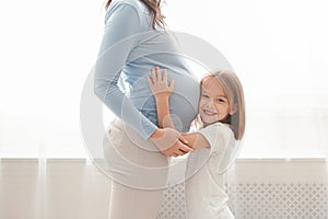 Little cute girl embracing her pregnant mother belly