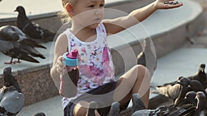 Little cute girl feeds pigeons near fountain