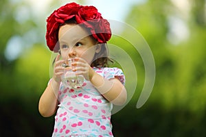 Little cute girl in flower wreath drinks milk in