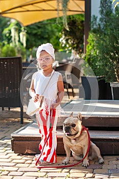 Little cute girl with french bulldog in a chair on the terrace of a cafe