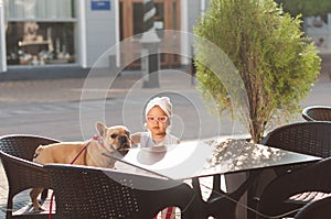 Little cute girl with french bulldog in a chair on the terrace of a cafe