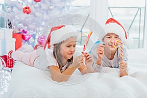 Little cute girl is frowning because she`ve broken her striped candycane. Her brother enjoys yummy lollipop.