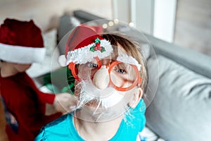 Little cute girl in funny glasses with nose, red Christmas santa claus hat. Congratulations,greetings. Kids, children playing on