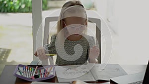 Little cute girl in glasses does homework while sitting at the table at home. The child learns English at home schooling