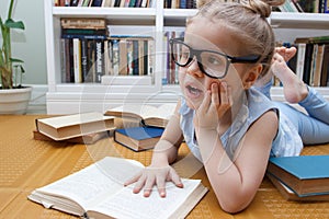 Little cute girl in the glasses sitting in the front of bookshelf. Concept of education