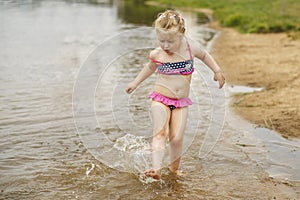 Little cute girl have fun playing with a spray of water in the river at summer. copy space