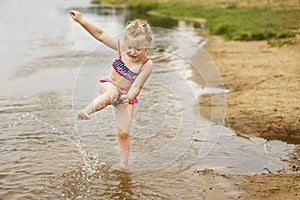 Little cute girl have fun playing with a spray of water in the river at summer. copy space